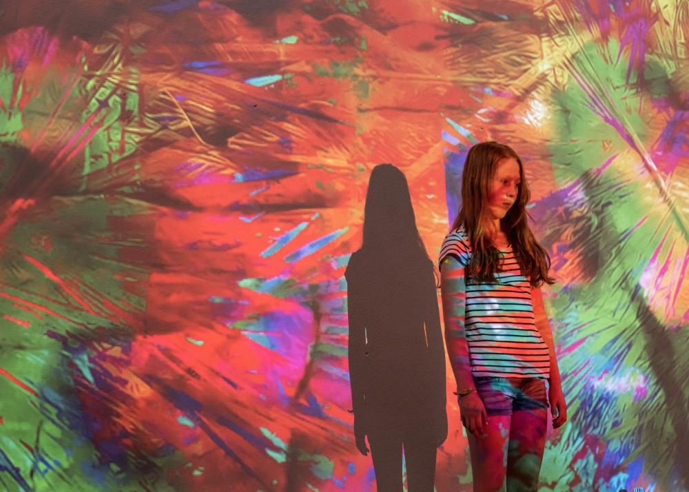 One girl standing alone, colors projected on the wall and her body.